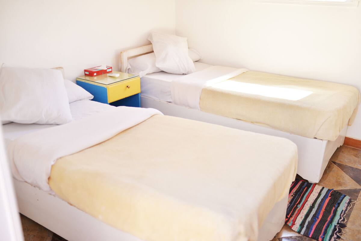 Ein Zimmer mit zwei Betten, einem Nachttisch und einem Fenster.