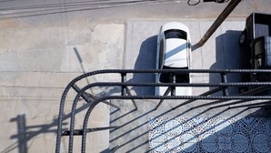 Guarda-corpo de metal com padrão geométrico, um carro branco estacionado em vaga demarcada e parede revestida com azulejos estampados.