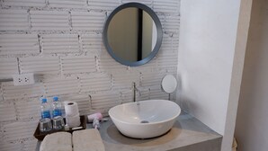 Casa de banho com parede de tijolo branco, espelho redondo, lavatório branco e toalhas numa bandeja.