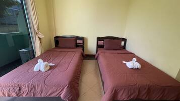 Two twin beds with matching brown bedding and pillows, a small trash bin, and a window with curtains.