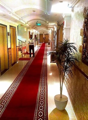 Corredor de hotel com carpete vermelho, planta em vaso e escada.