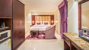Une chambre d’hôtel comprenant un lit, une chaise, une petite table, une armoire, un four à micro-ondes et une coiffeuse avec un miroir.