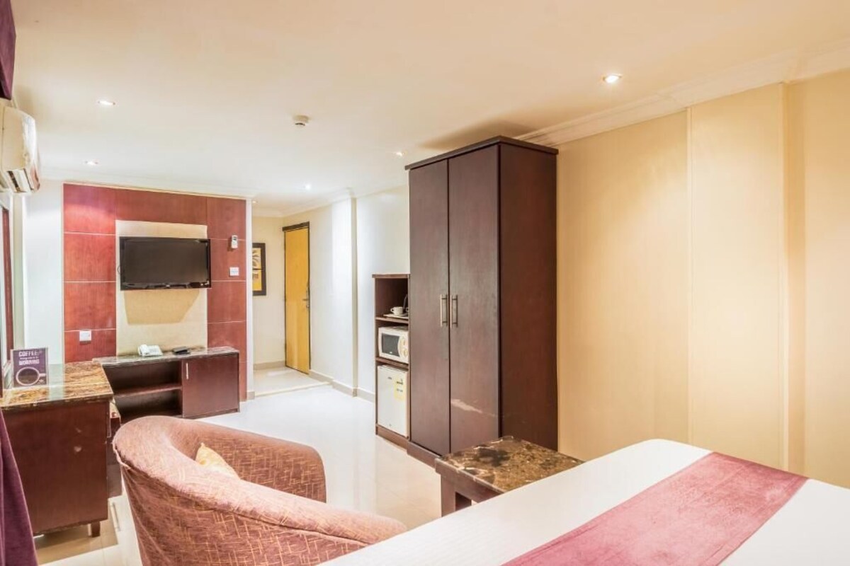Habitación de hotel con cama, escritorio, silla, armario y televisión.