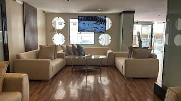 Un área de estar moderna con sofás, una mesa de centro de vidrio y una pantalla de televisión grande.