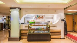 Un espace d’accueil comprenant un présentoir en verre contenant des collations et des boissons, un comptoir de réception et un tapis rouge menant à une porte.