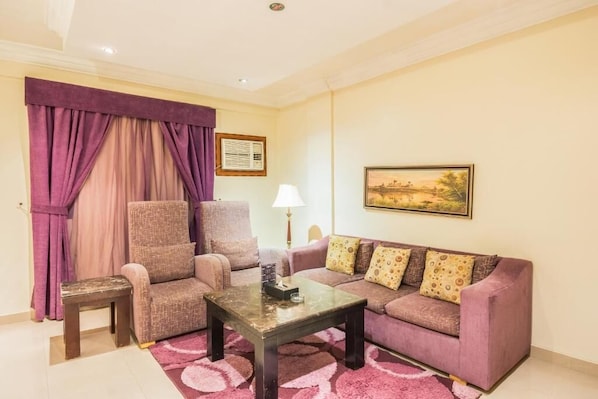 A living room with a sofa, armchair, coffee table, and a lamp. - Nawara Takhasossi - Economic (Riyadh)