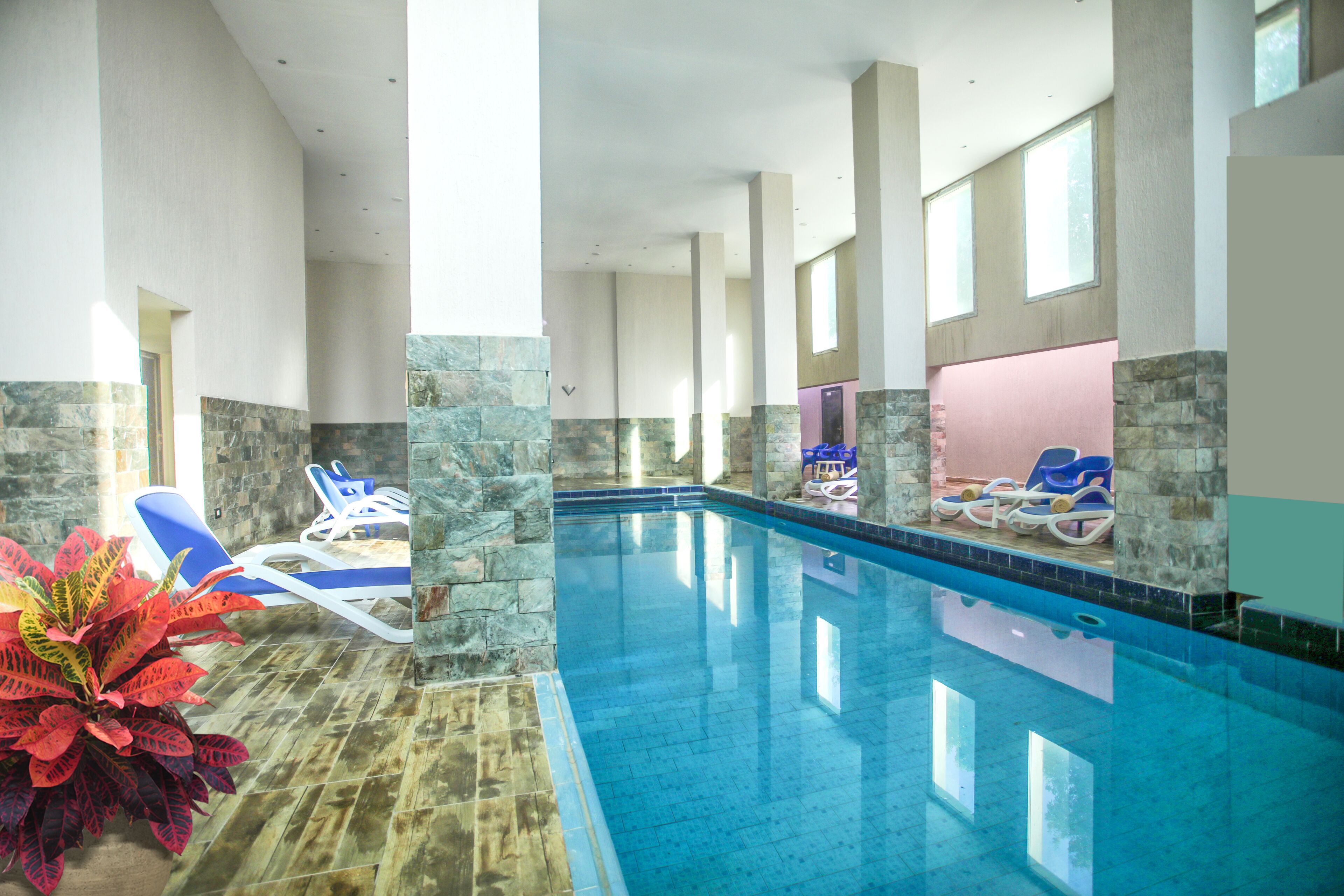 An indoor swimming pool with clear blue water, surrounded by stone walls and columns, and equipped with lounge chairs.