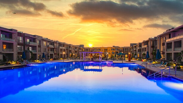 Une piscine d’hôtel offrant une vue sur le coucher de soleil, entourée d’immeubles à plusieurs étages dotés de balcons.
