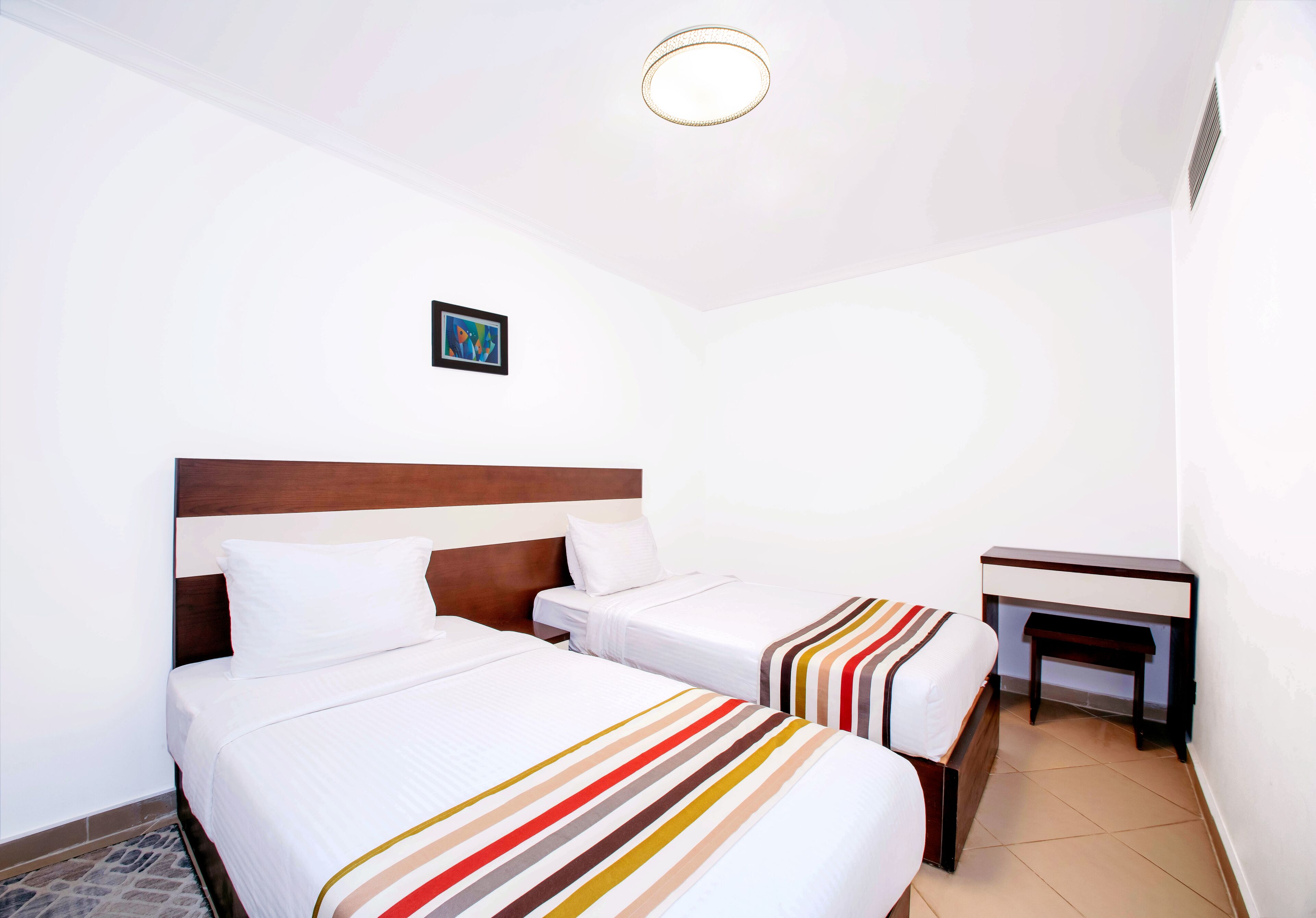 Een hotelkamer met twee bedden, een klein bureau en een plafondlamp.