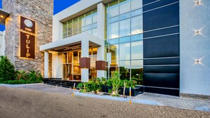 Une entrée d’hôtel moderne avec une façade en pierre, de grandes fenêtres en verre et une enseigne bien éclairée.