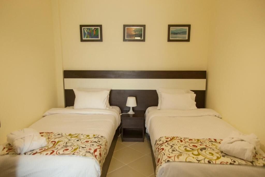 A hotel room with two single beds, a nightstand with a lamp, and three framed pictures on the wall.