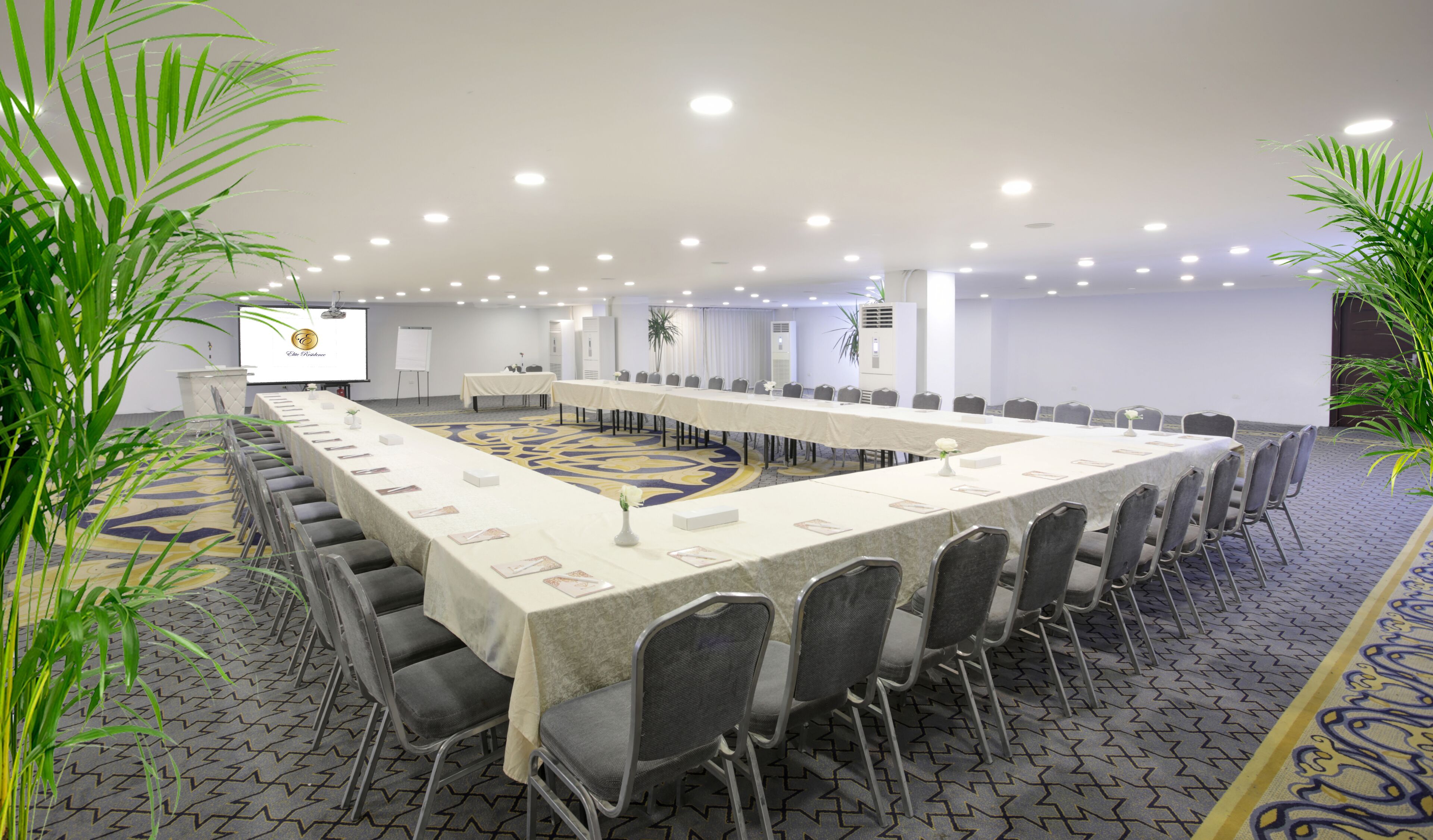 Un salón de conferencias con una larga mesa, sillas y una pantalla para proyector.
