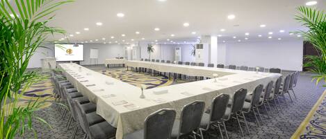 Un salón de conferencias con una larga mesa, sillas y una pantalla para proyector.