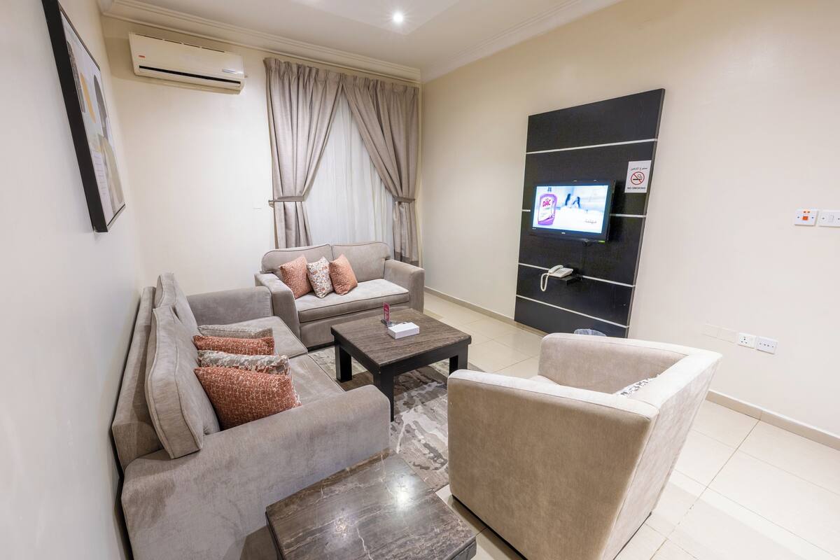 Un salon moderne comprenant un canapé, des fauteuils, une table basse et un téléviseur à écran plat fixé au mur.