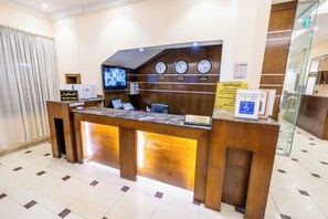 A reception desk with a digital screen, clocks, and signs indicating a disabled room and departure time.