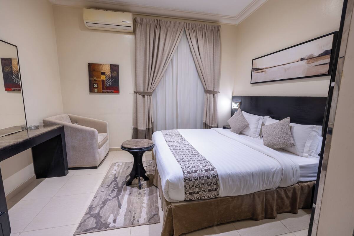 Une chambre d’hôtel avec un lit, un bureau, une chaise, un climatiseur et un tableau au mur.