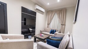 A modern living room with a flat-screen TV, beige sofas, a coffee table, and an air conditioning unit. - Nawara AL  ASKARY - Economic (Riyadh)