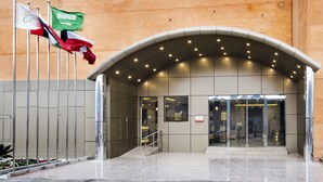 A modern building entrance with a curved overhang and multiple flags. - Al Muhaidb Residence Serviced Apartments (Al-Hofuf)