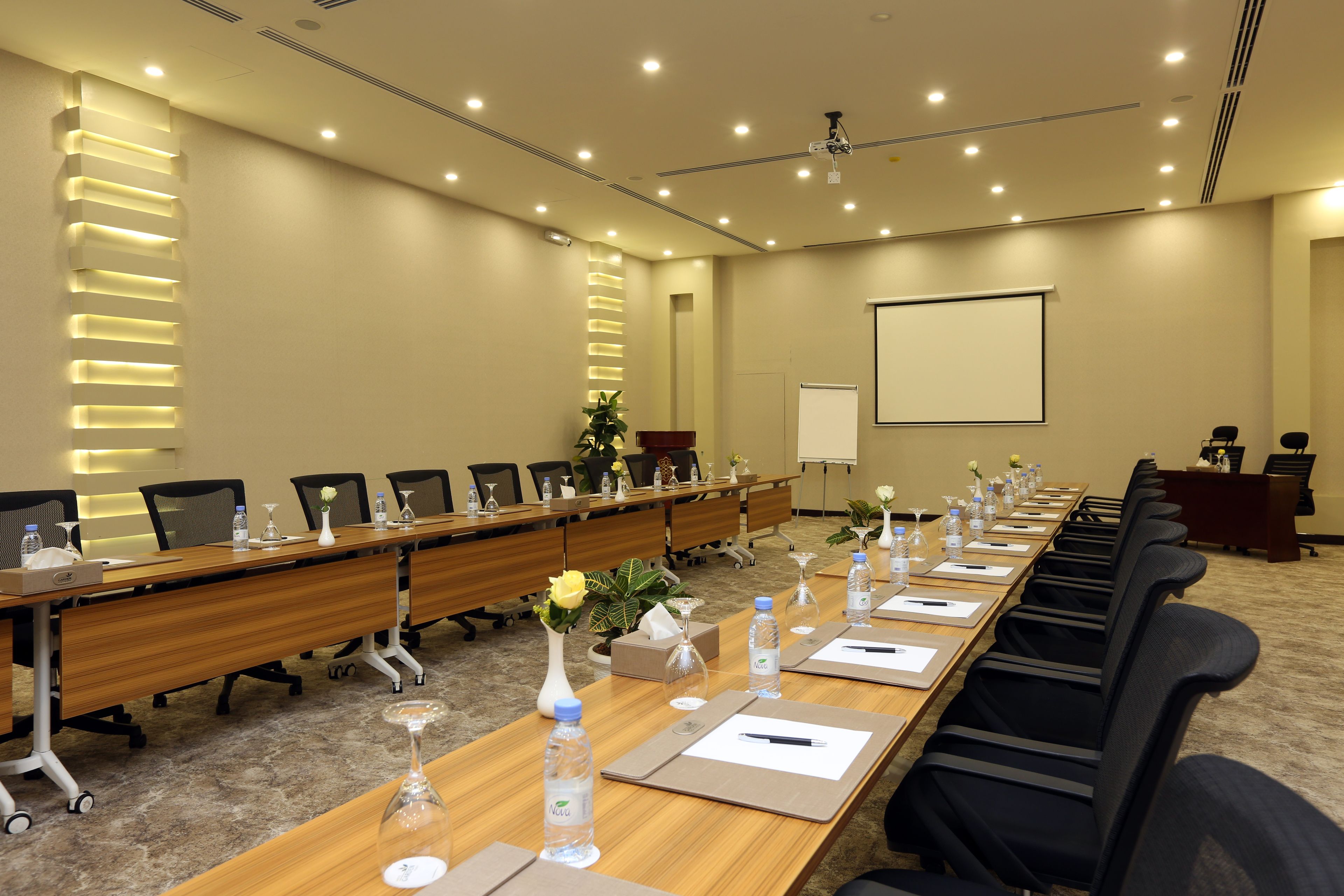 A conference room with a long table, chairs, water bottles, and a projector screen.