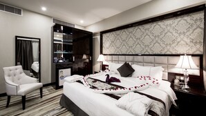 A hotel room with a large bed, a sitting area with a chair, a vanity with a mirror, and a dresser. - Al Muhaidb Residence Serviced Apartments (Al-Hofuf)