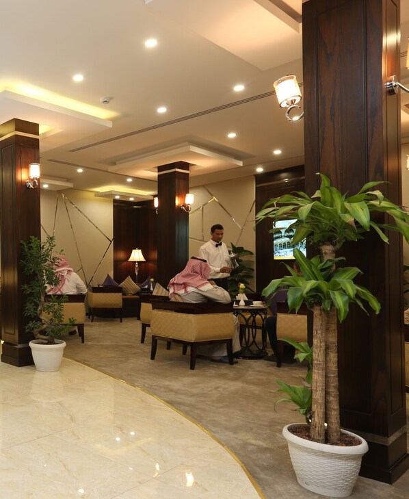 A hotel lobby with a marble floor, wooden furniture, and potted plants.