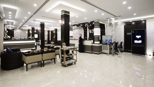 A modern hotel lobby with a reception desk, seating area, and a digital information display. - Al Muhaidb Residence Serviced Apartments (Al-Hofuf)