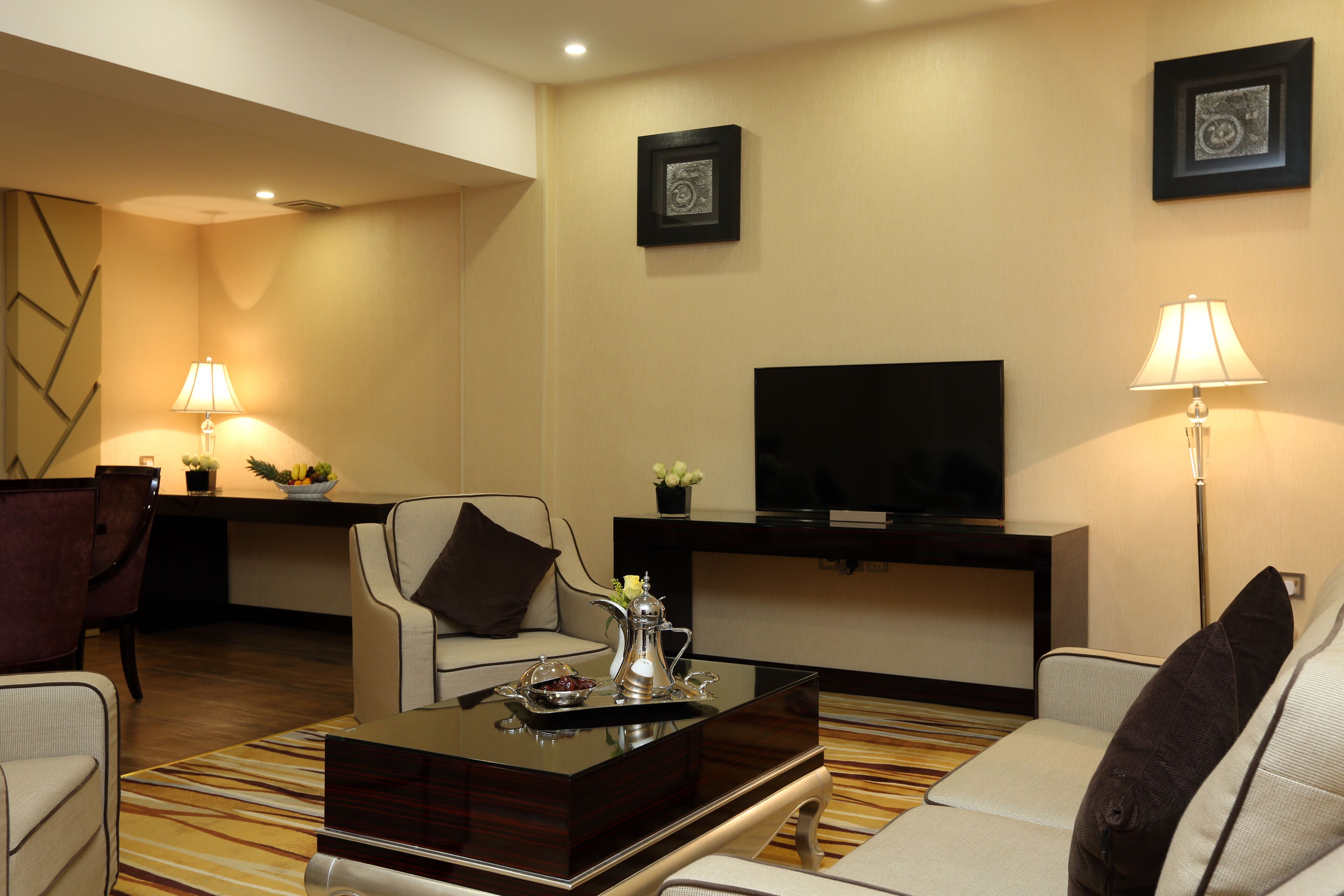 A modern living room with a sofa, armchairs, a coffee table, a flat-screen TV, and two lamps.