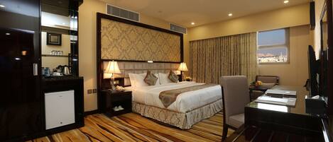 Habitación de hotel con cama, escritorio, silla, refrigerador pequeño y ventana con vista a la ciudad.