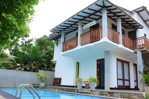 Une maison à deux étages avec un balcon, une piscine et des plantes en pot.