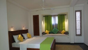 Ein Schlafzimmer mit einem Bett, einer Fensterbank mit Kissen, einem Deckenventilator und Blick ins Freie.