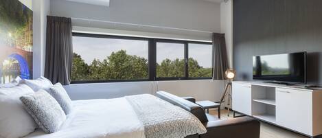 Une chambre d’hôtel moderne, dotée d’un grand lit, d’un bureau, d’une télévision et offrant une vue sur l’extérieur.