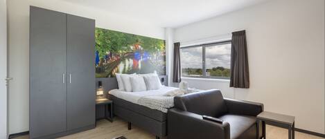 A modern hotel room with a bed, a sofa, a small table, and a wardrobe.