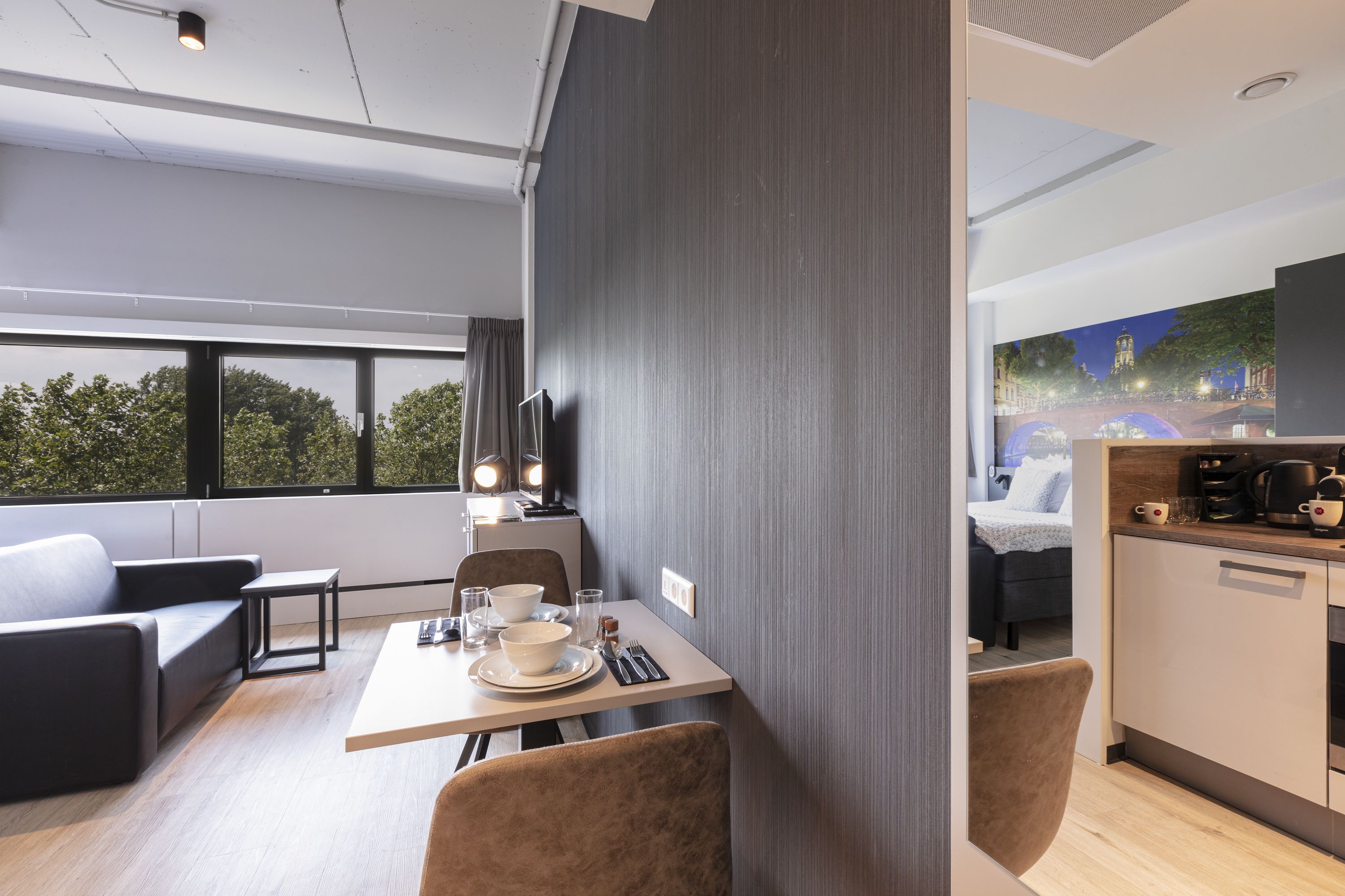 Una habitación de hotel moderna con zona de comedor, sofá, una mesita y espacio para la cocina.