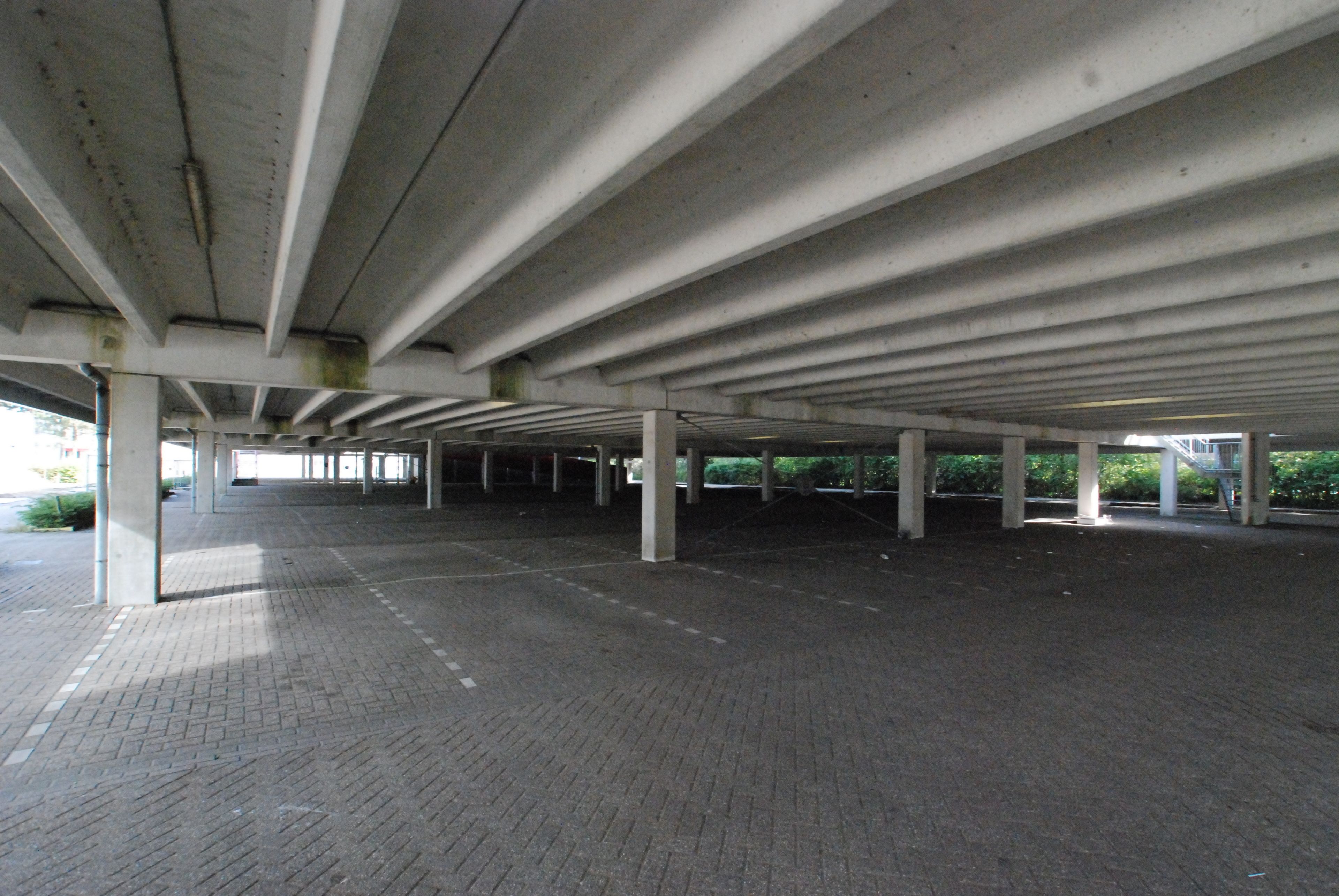 Una estructura subterránea de estacionamiento con pilares de hormigón y suelo de baldosas.