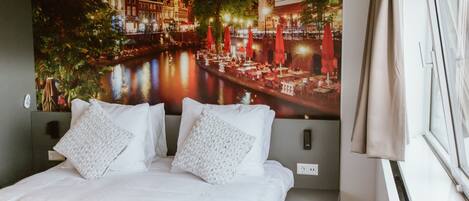 A hotel room with a large bed, two pillows, a bedside table, and a window with curtains.