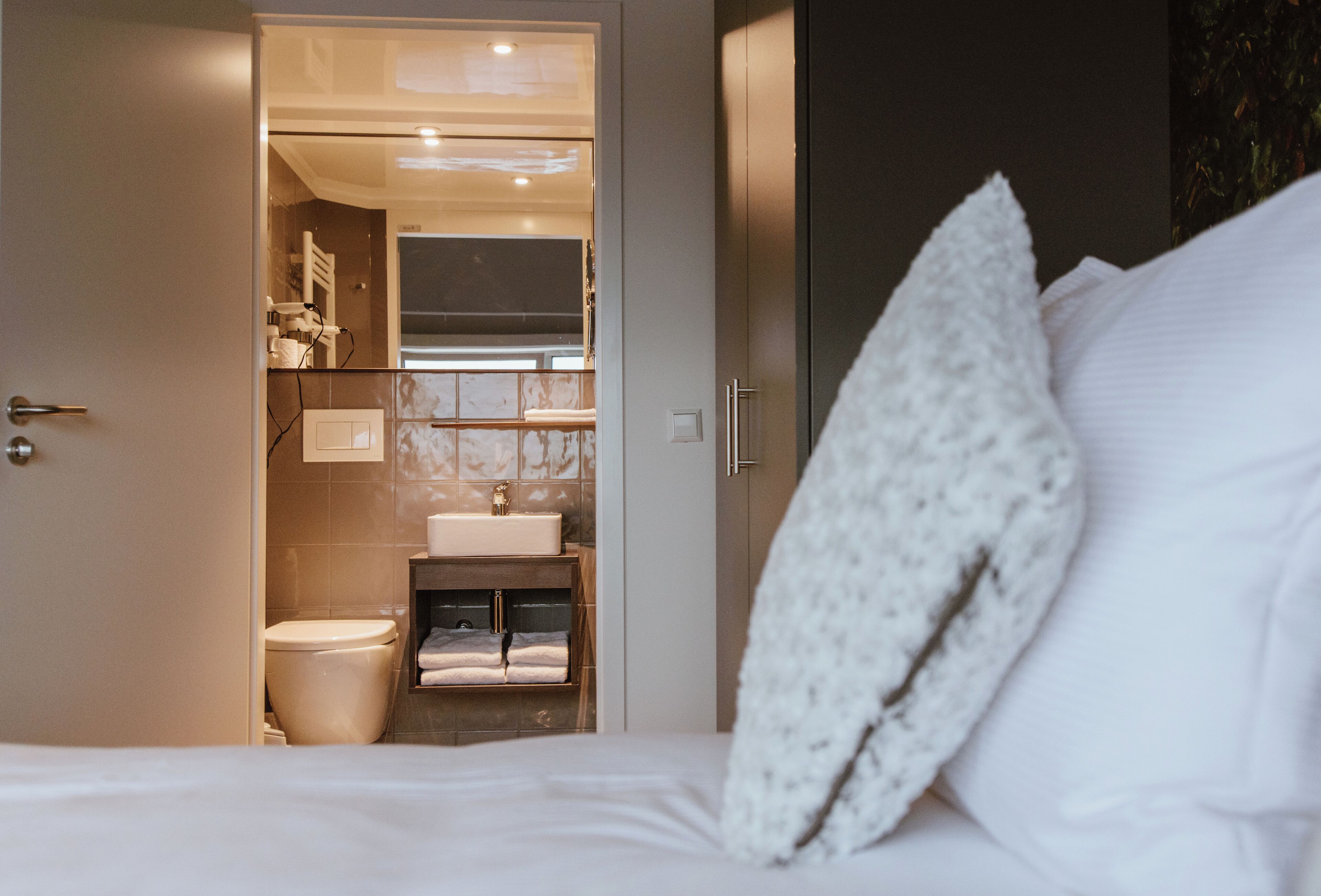 Et hotelværelse med en seng, en hvid pude, et badeværelse med toilet, vask og håndklædestang.