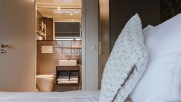 Et hotelværelse med en seng, en hvid pude, et badeværelse med toilet, vask og håndklædestang.