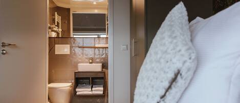 Hotelkamer met een bed, een wit kussen, een badkamer met toilet, wastafel en handdoekhouder.