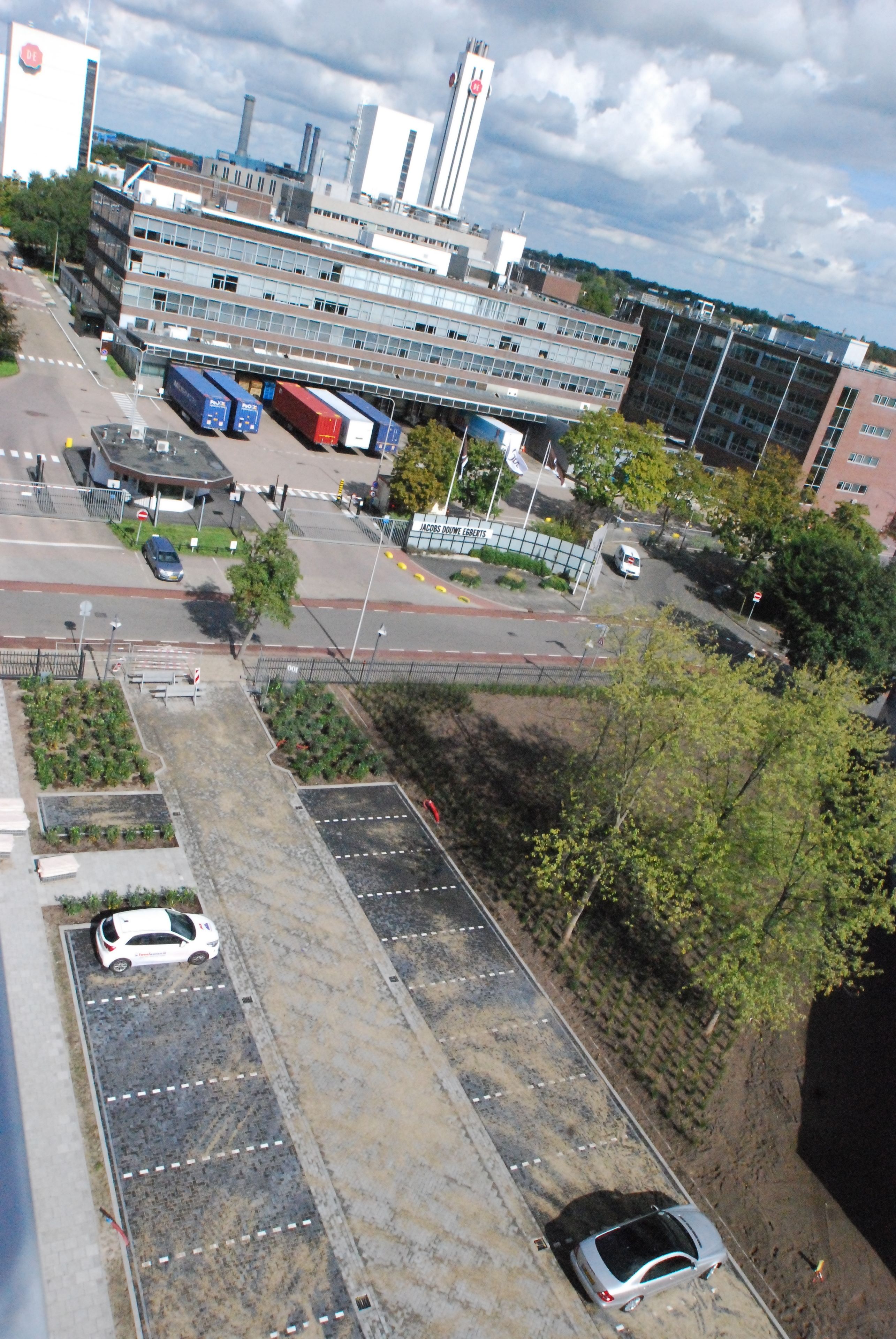 Une vue aérienne d’un parking où se trouvent plusieurs voitures, un autobus et un immeuble à étages avec de grandes fenêtres.