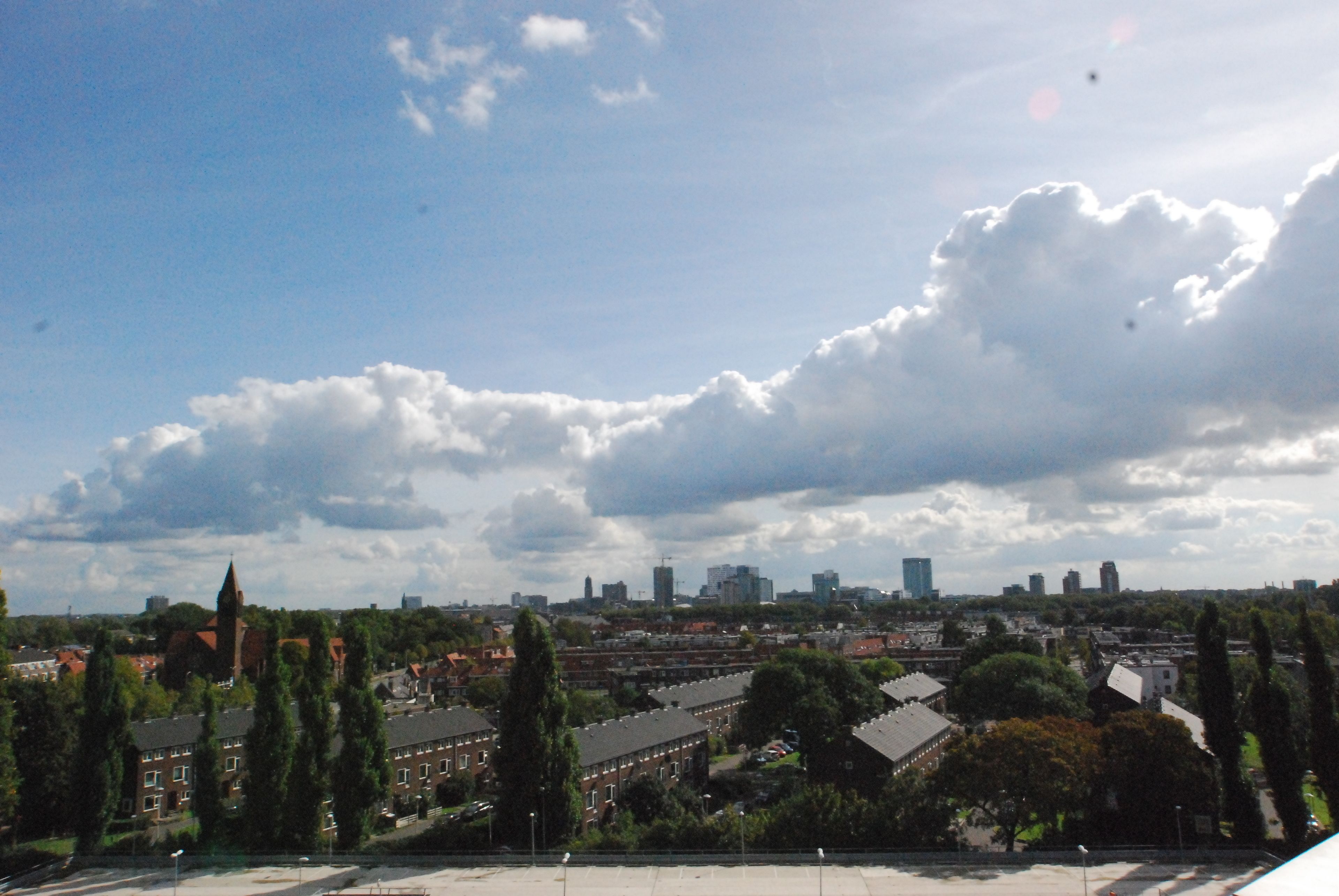 Un paysage urbain avec des immeubles résidentiels, un clocher d’église imposant et une silhouette de gratte-ciel modernes.