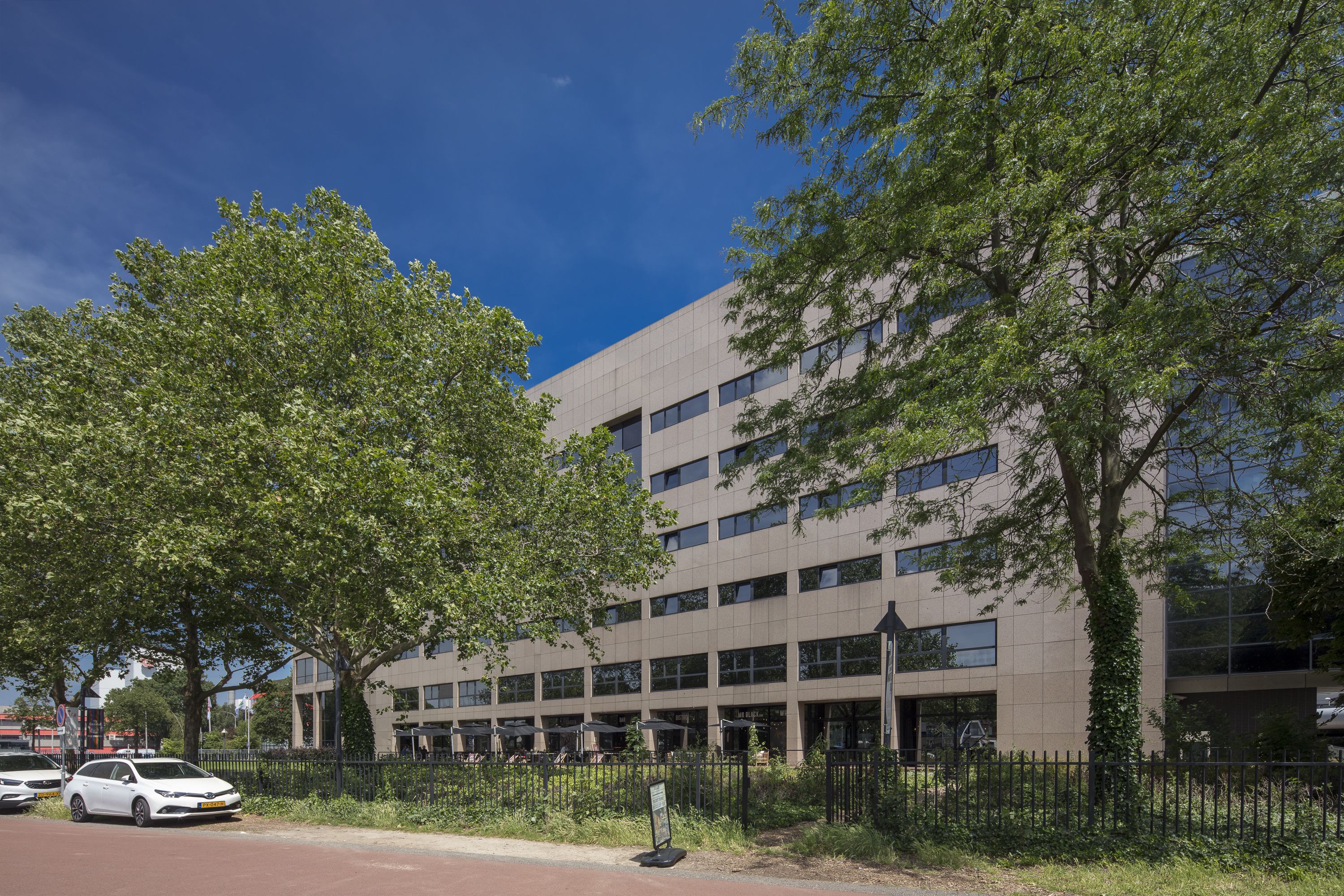 A modern building with multiple floors, large windows, and a surrounding fence.
