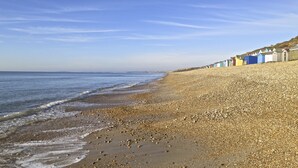 Ein Kiesstrand mit einer Reihe bunter Strandhäuser auf der rechten Seite.