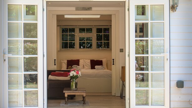 Ein Zimmer mit einem Bett, einem kleinen Tisch mit Blumenvase und einem Fenster mit einem Rauchverbot-Schild darüber.