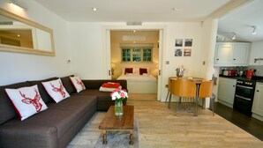 Ein Wohnzimmer mit einer Couch, Couchtisch und einem Essbereich mit Tisch und Stühlen. Im Hintergrund ist eine Küche zu sehen.