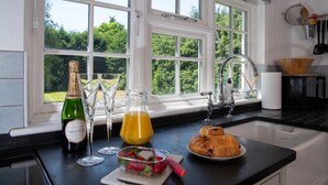 Eine Küche mit einem großen Fenster, einer Champagnerflasche, einem Orangensaftglas, einem Teller mit Croissants und einem Schneidebrett mit Erdbeeren.