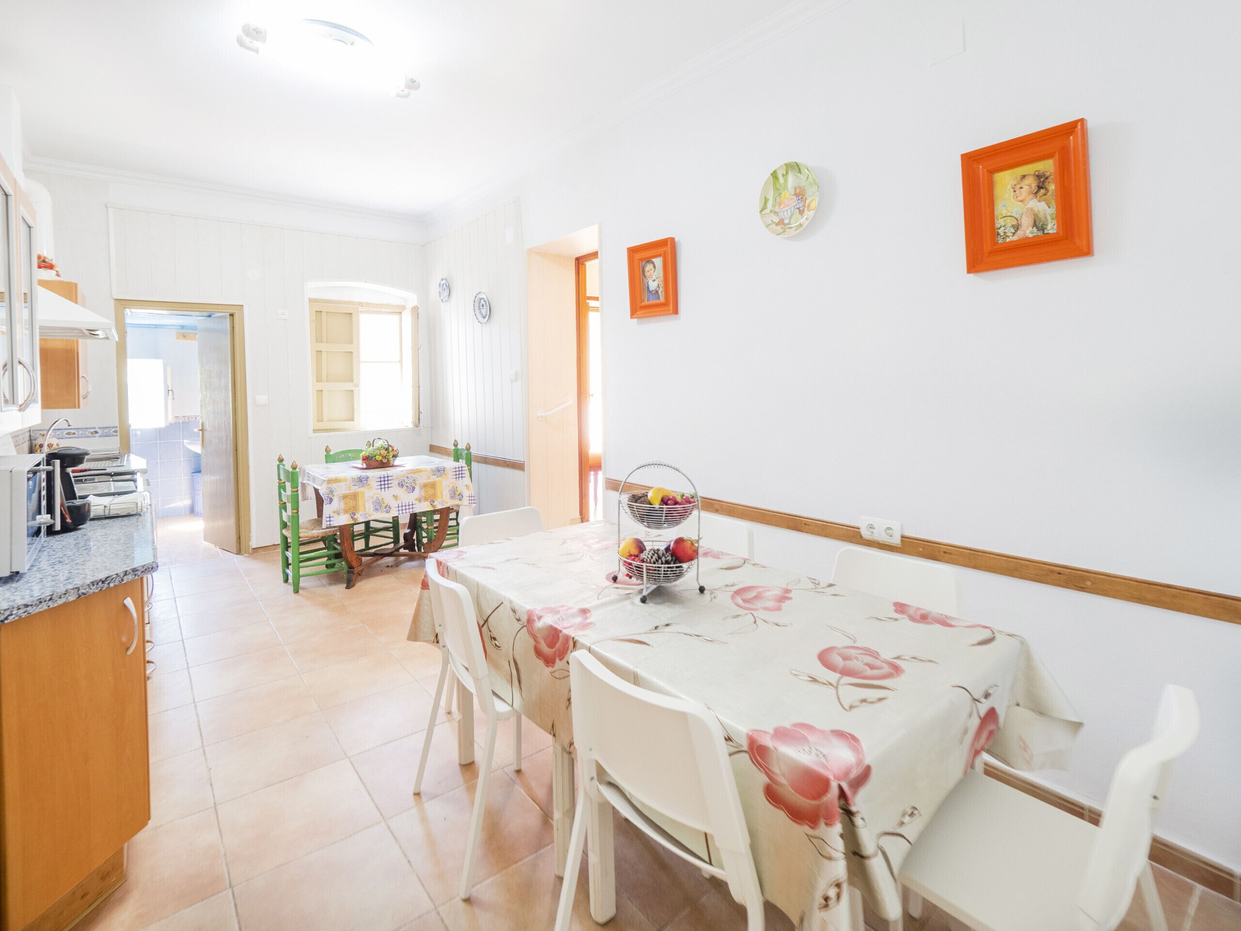 A dining area with a table set for four, a kitchen in the background, and a door leading to another room.