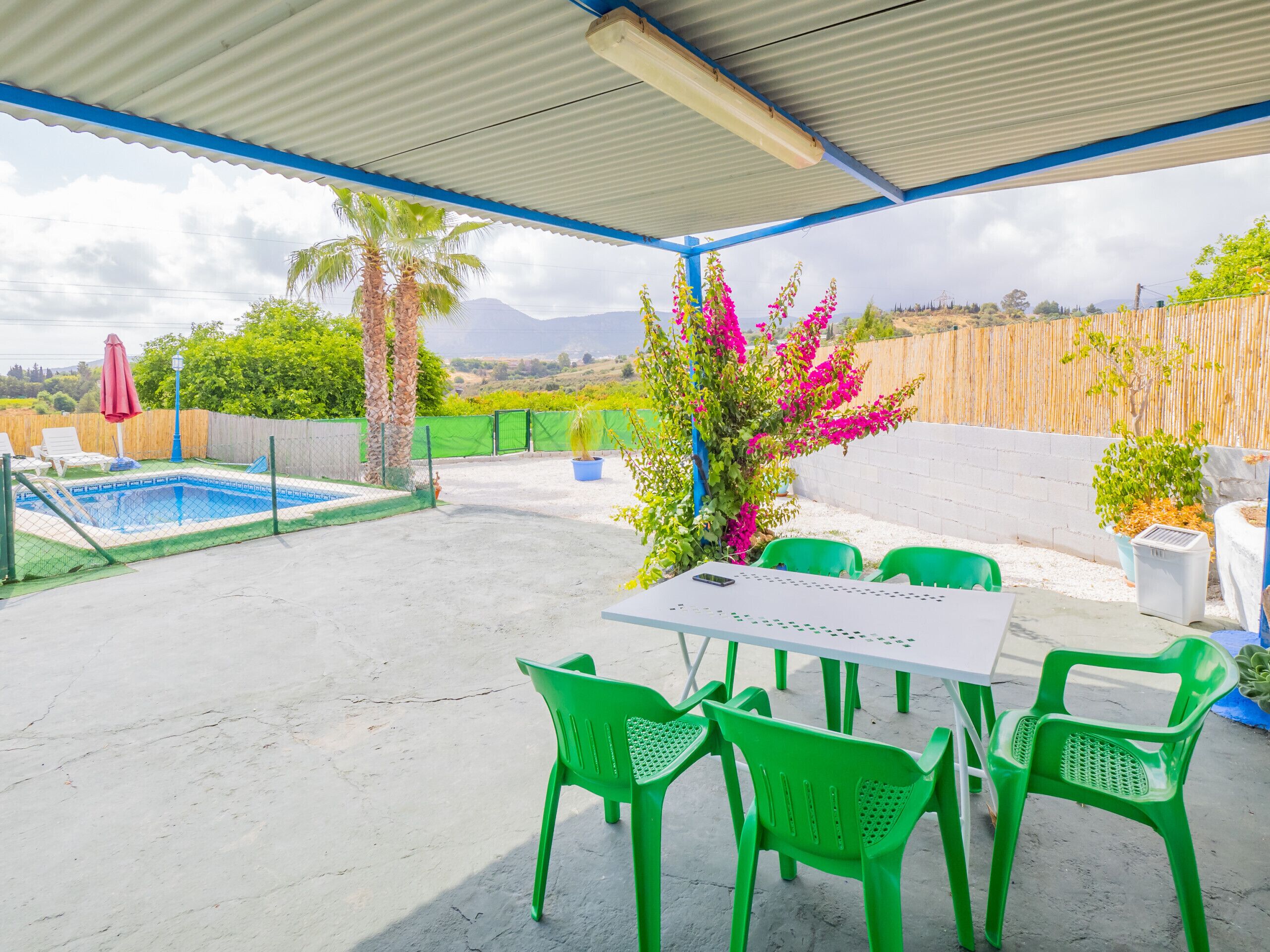 A covered outdoor area with a pool, green chairs, and a table.