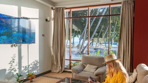 A living room with a sofa, armchair, and a coffee table. There is a ceiling fan, a TV mounted on the wall, and a window with curtains. - Silver Oasis Maldives (Huraa)