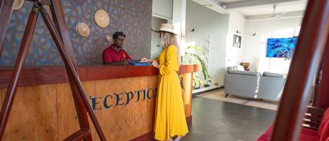 A reception area with a wooden reception desk labeled "RECEPTION," a man in a red shirt, and a woman in a yellow dress.