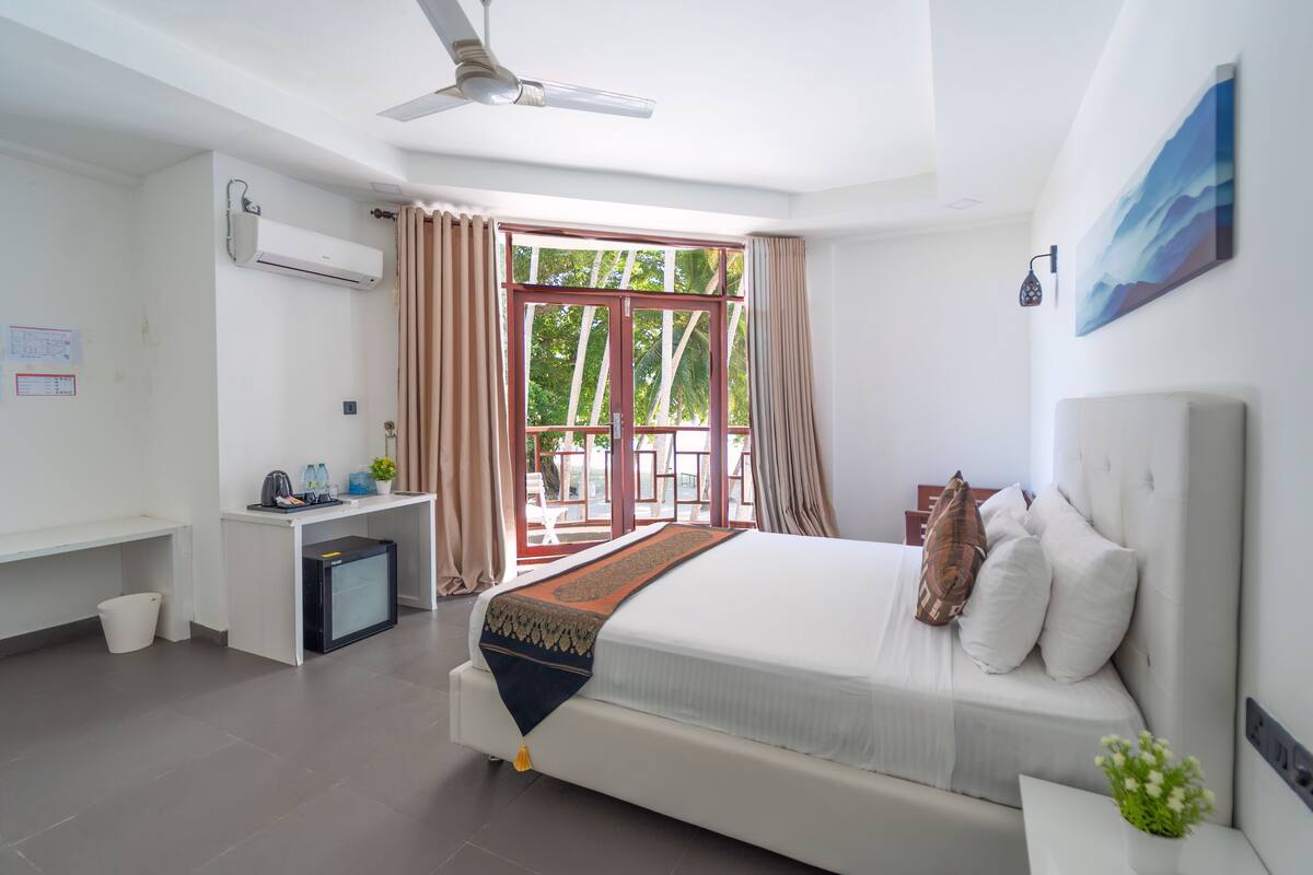 A hotel room with a bed, desk, air conditioning unit, and a window with curtains.
